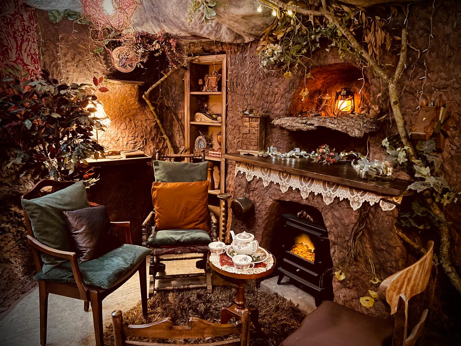 The cosy Beaver's Den cave interior at Cedar Hollow, with a glowing lantern, fireplace and afternoon tea by the fire