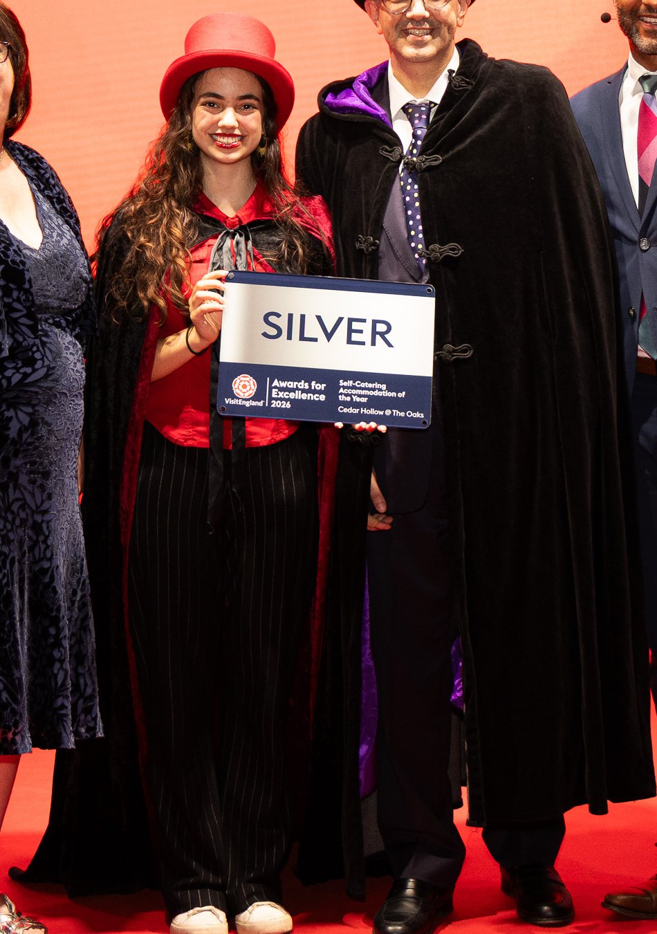 Miss Direction in a red top hat and cape at the VisitEngland Awards for Excellence, holding the Silver award plaque