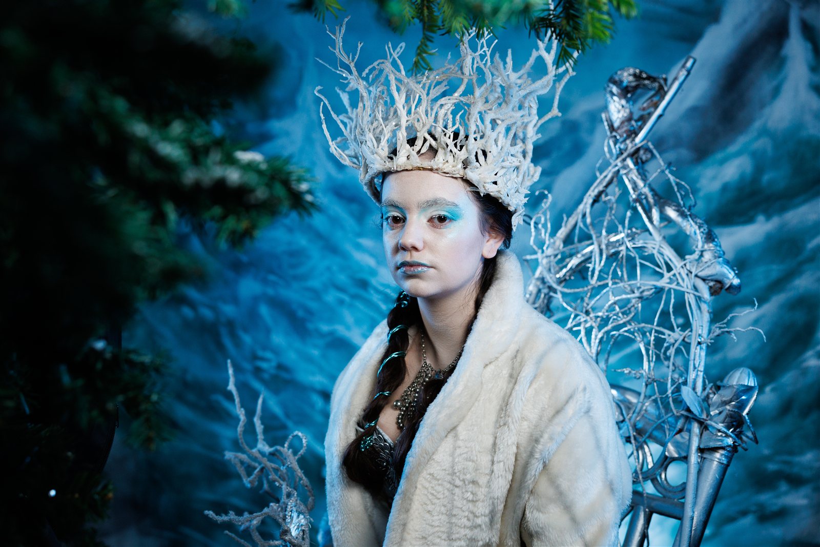 The White Queen seated on a silver throne in a frozen woodland, wearing a white fur coat and a crown of frosted branches