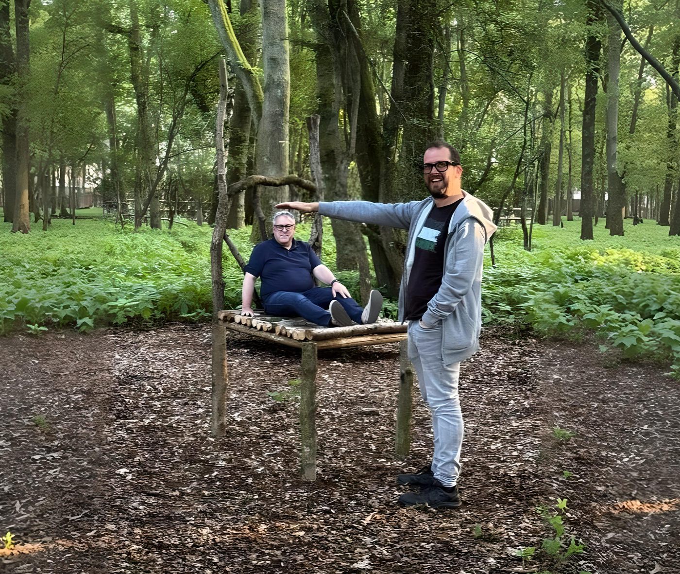 Two people demonstrating the Beuchet Chair illusion. One sits tiny on the seat while the other stands giant beside the chair