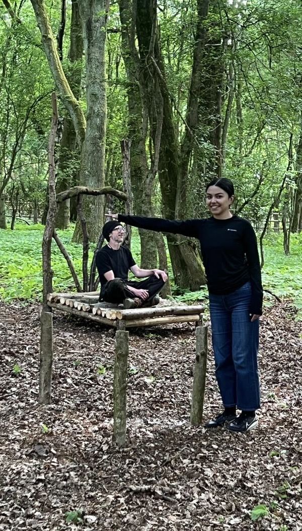A child appears tiny on a forced-perspective chair while an adult stands next to it at full size