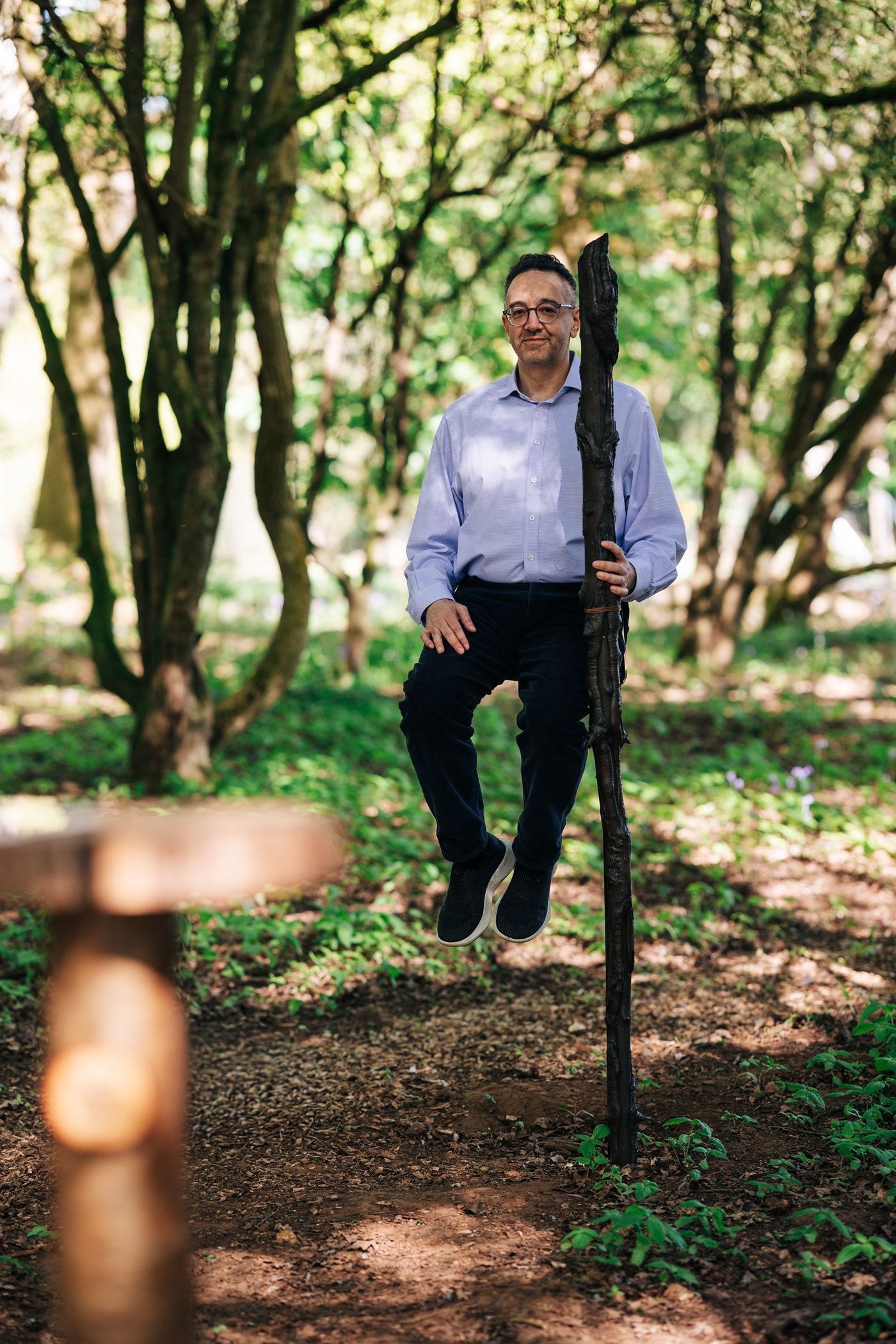 A man appears to levitate while leaning on a wooden staff in the woods