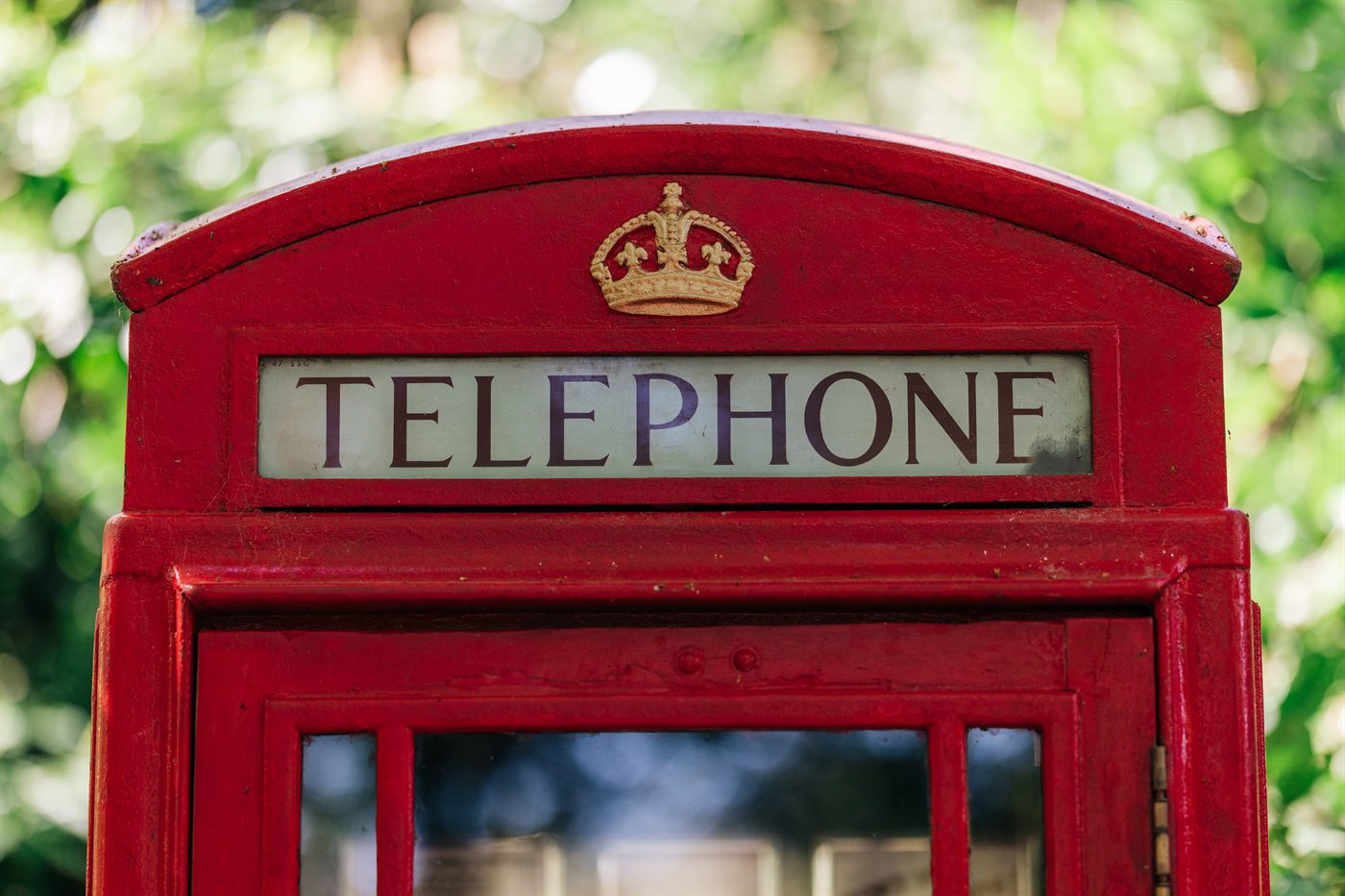 A close-up of the red 1920s telephone box, showing the gold crown emblem and the iconic TELEPHONE sign at its top. This is the K6 design, originally specified by the General Post Office in the 1930s and updated from Sir Giles Gilbert Scott's 1924 K2.